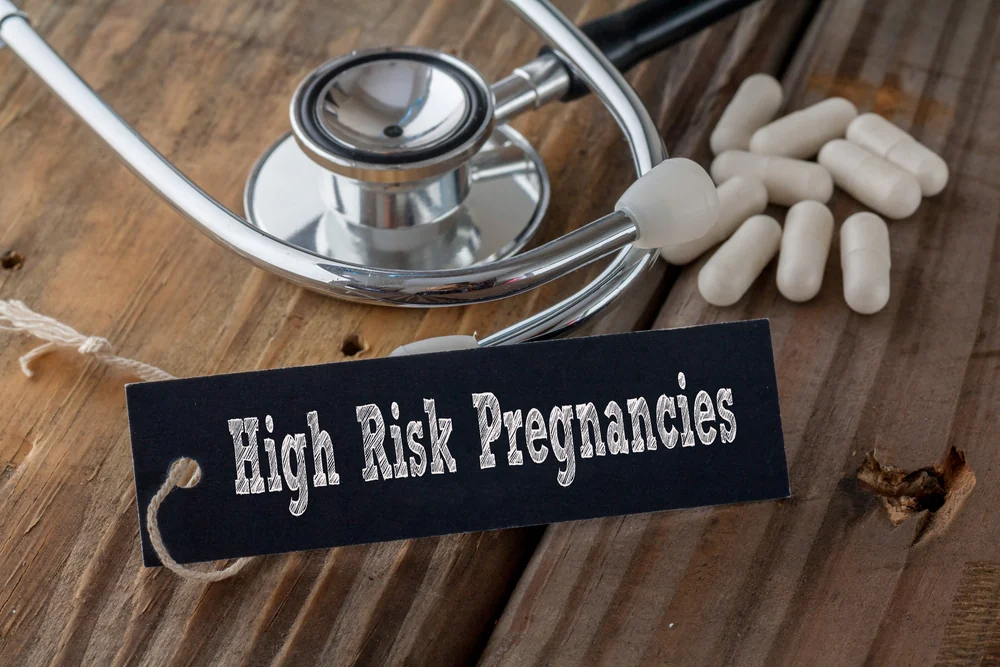 A chalkboard sign reading High Risk Pregnancies, resting on a wooden surface beside a stethoscope and tablets.